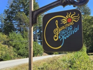A photo of a hand-painted sign that is posted on the highway; it says "Sunshine Music Festival"