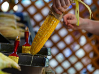 A photo of a cob of corn being smothered with butter over a tray