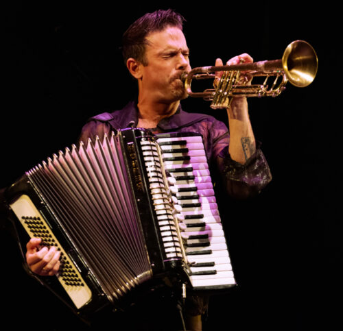 Jack Garton performing with his accordion while blowing his trumpet.