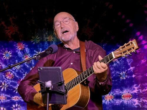 A photo of Pat Buckna singing and playing guitar live.